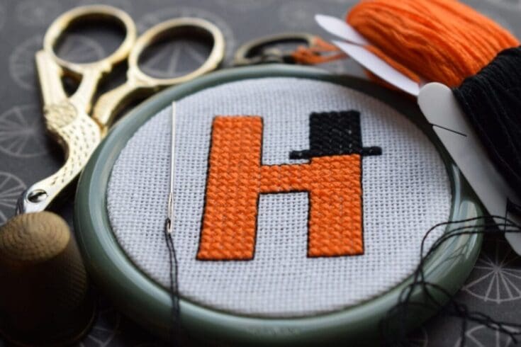 embroidered h is for hat cross stitch pattern in a flat lay with embroidery tools and threads
