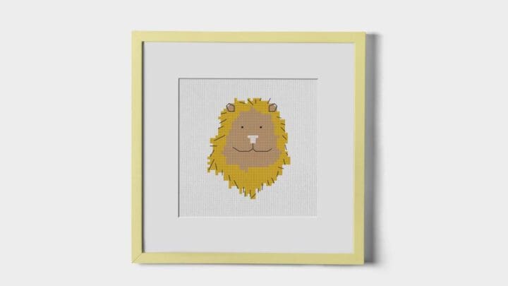 Framed cross stitch pattern of a lion stitched, hung on a white wall