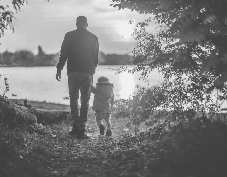 black and white image of father and son walking away to a lake