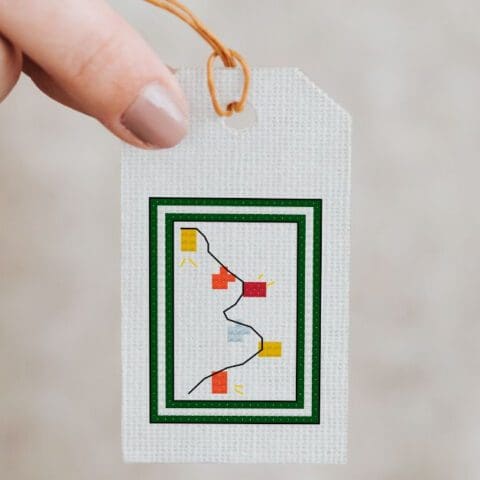 close up of womans hand holding a christmas cross stitch gift tag pattern sewn up.