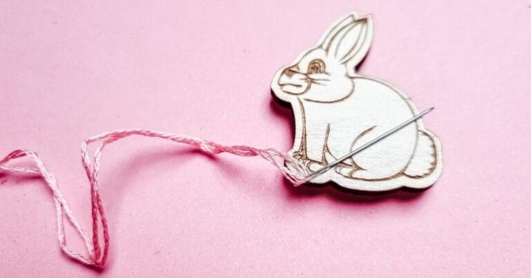 rabbit needle minder on a pink background holding a needle with a pink thread