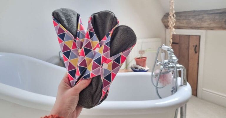 3 reusable sanitary pads being held in one hand in a bathroom for review