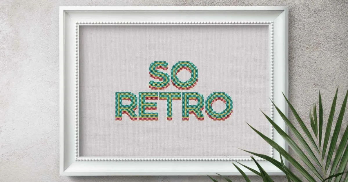 Image shows the so retro cross stitch pattern embroidered on to white fabric, framed in a white frame hung on a wall with a palm plant next to it.