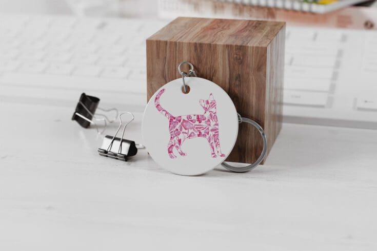 image shows a white key chain with a silhouette of a cat filled with begonia rex leaves sublimated on to it.