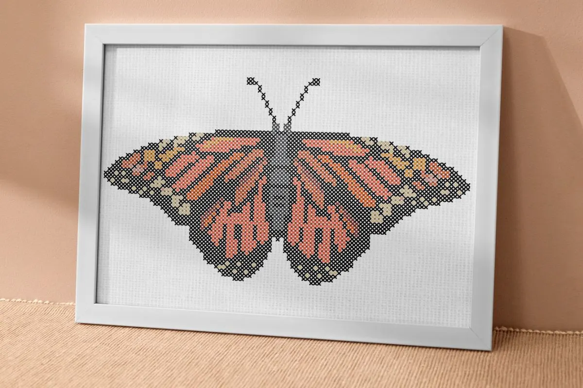 an embroidered monarch butterfly cross stitch pattern framed in a white rectangle frame