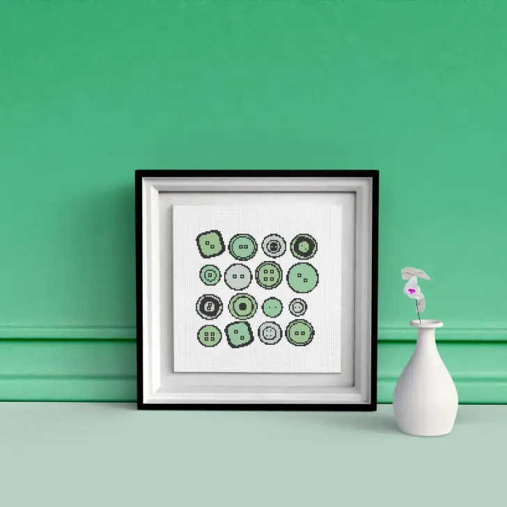 image shows embroidered green buttons cross stitch, framed in a black square frame against a green wall