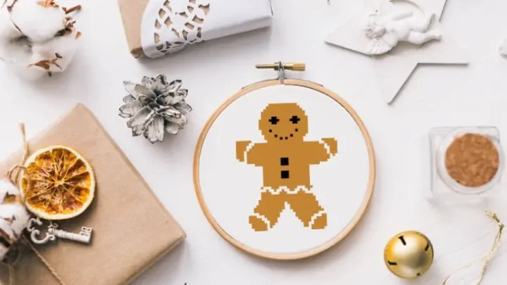embroidered and framed in a hoop gingerbread man cross stitch surrounded by christmas decorations
