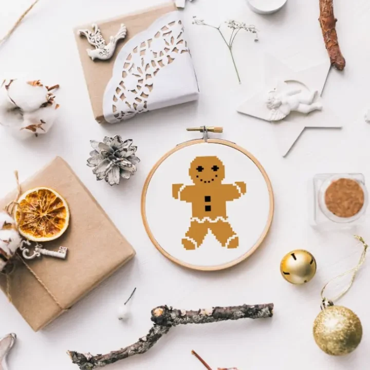 embroidered and framed in a hoop gingerbread man cross stitch surrounded by christmas decorations