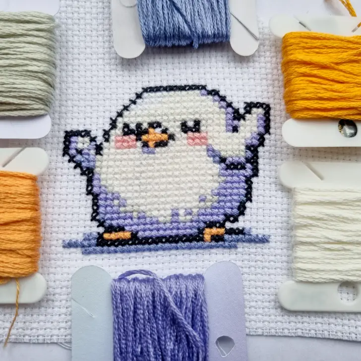 chubby bird cross stitch surrounded by floss bobbins of the colours stitched