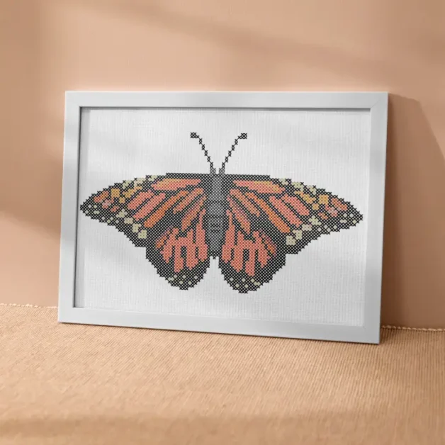 an embroidered monarch butterfly cross stitch pattern framed in a white rectangle frame