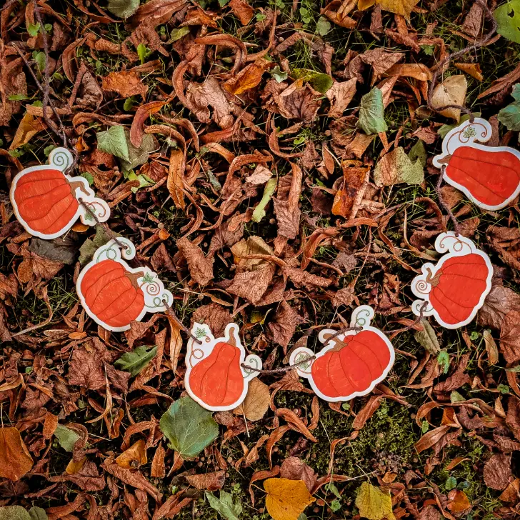 a diy laser cut wooden pumpkin garland lay on a lawn of fallen autumn leaves