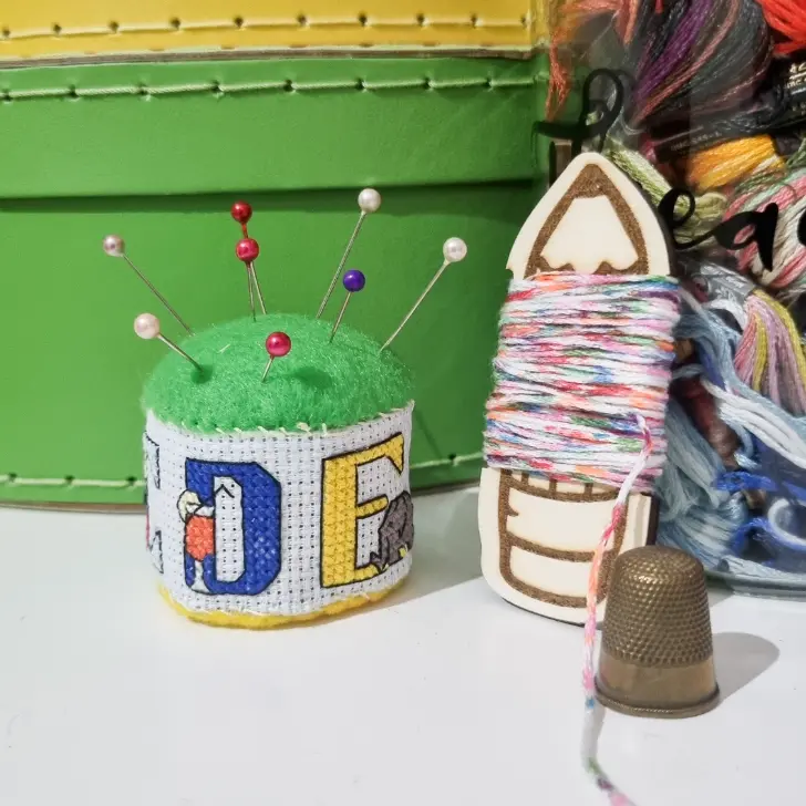 cross stitch pin drum displayed with a thimble and a bobbin of floss